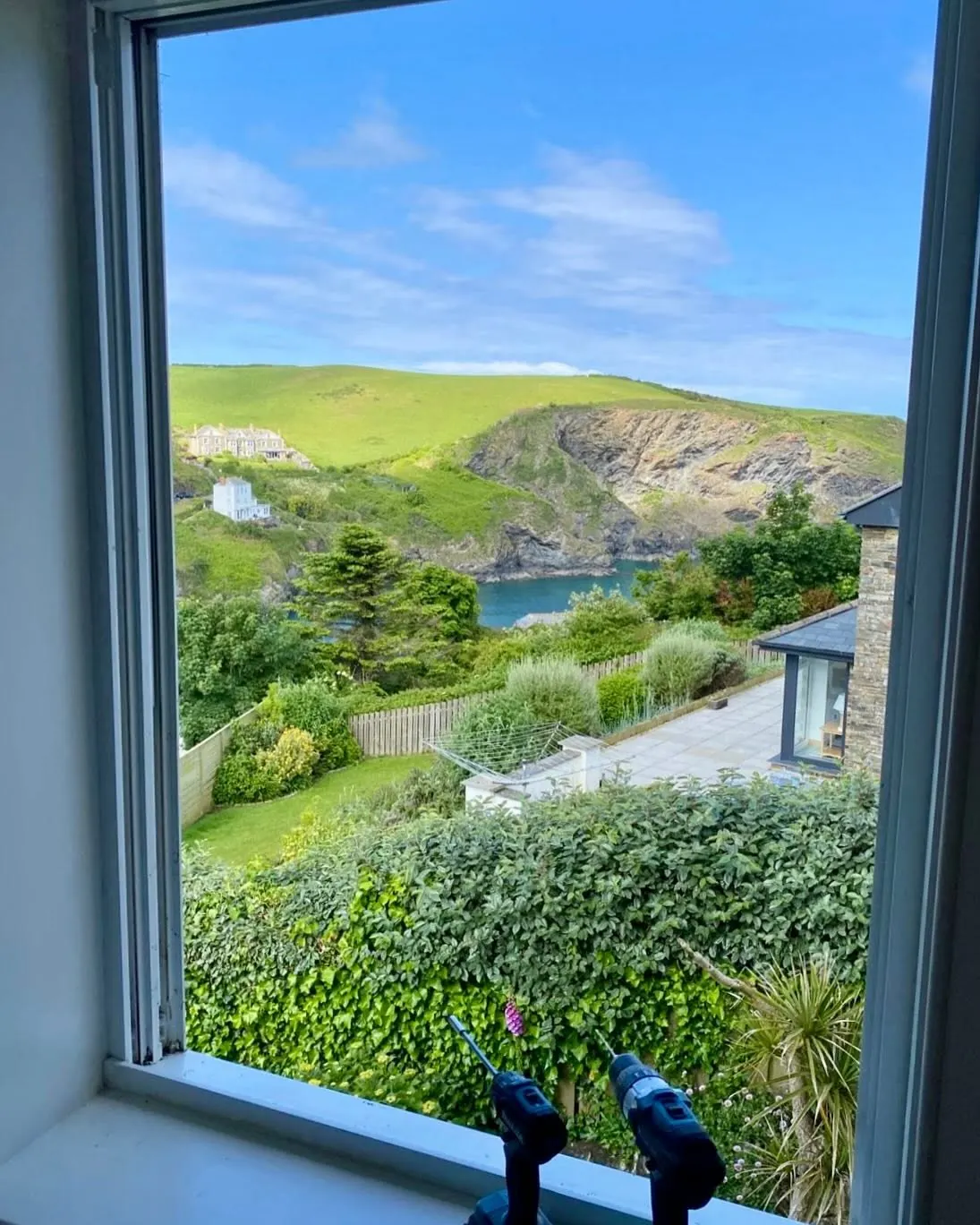 View through a newly repaired window over a green Cornish valley to the sea